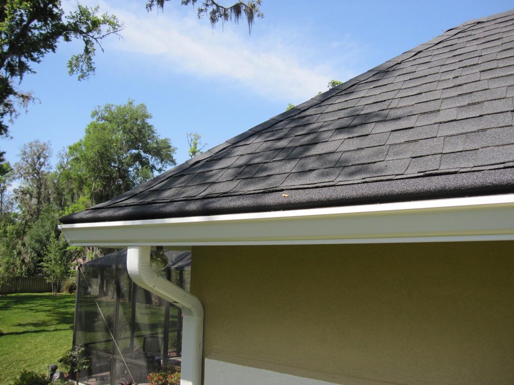 Dark shingle roof edge with white gutter on a stucco home