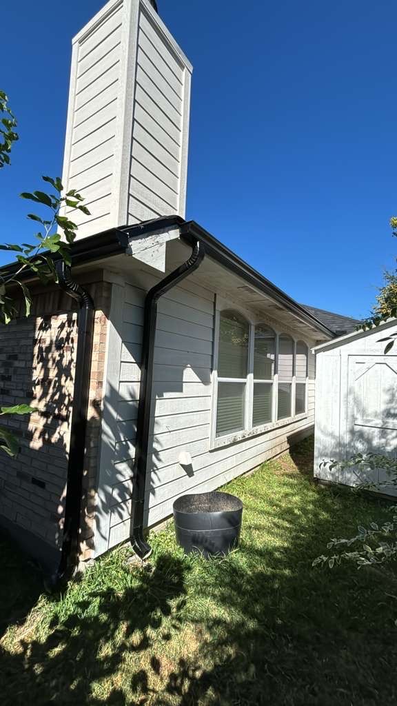 Black seamless gutter and downspout installed on a home with white siding