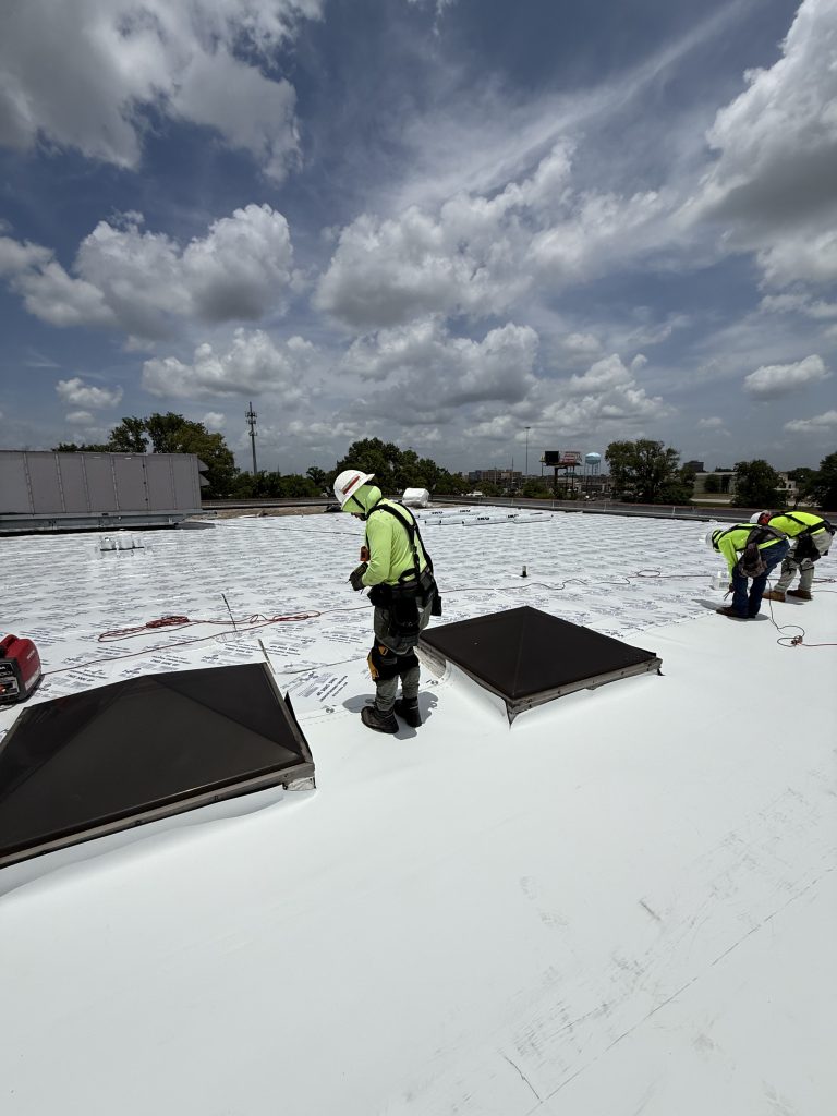 Roofer installing a white flat roof around skylights on a commercial building