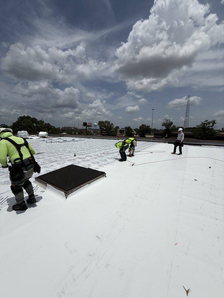 Roofing crew installing a white flat roof around skylights