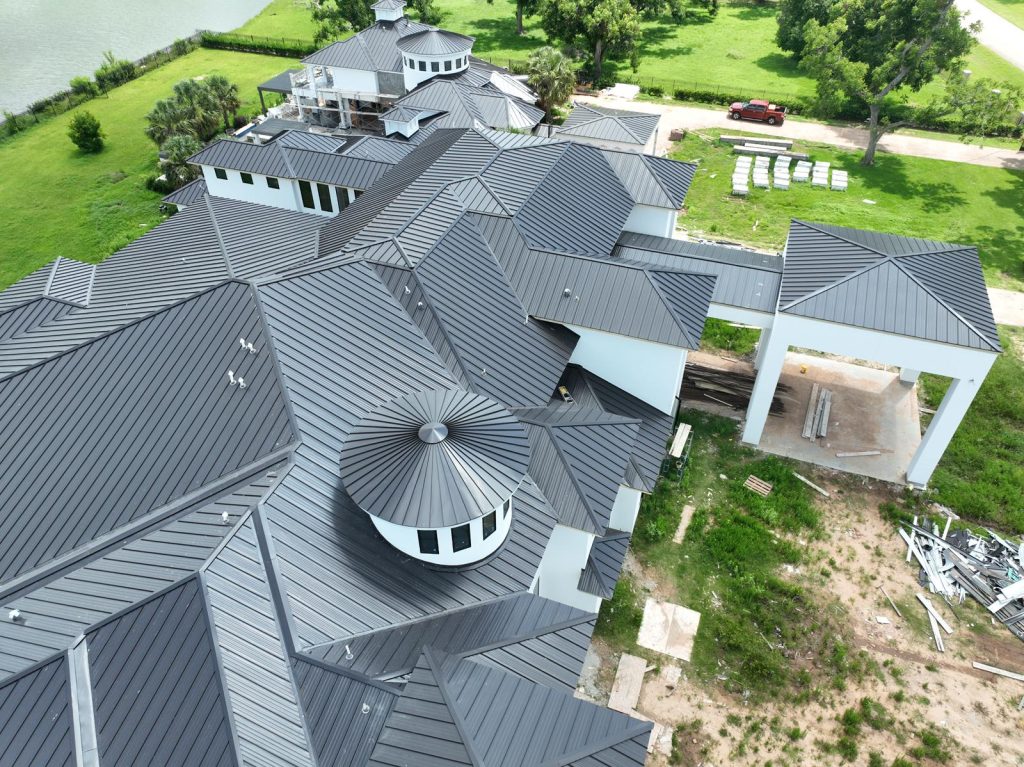 Aerial view of a new standing seam metal roof with a round turret on a large lakeside home